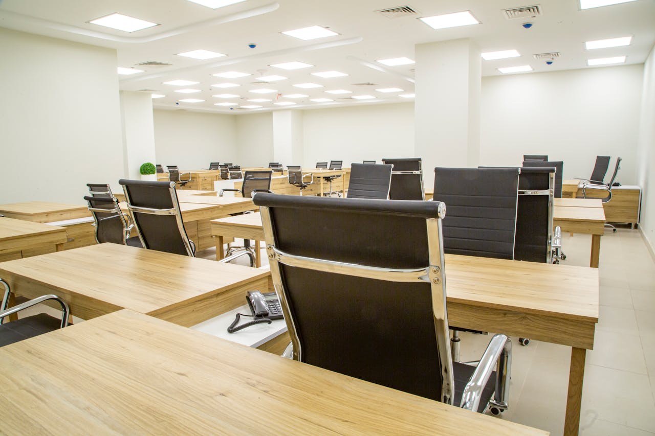 Spacious modern office with wooden desks and leather chairs in a bright, well-lit room.
