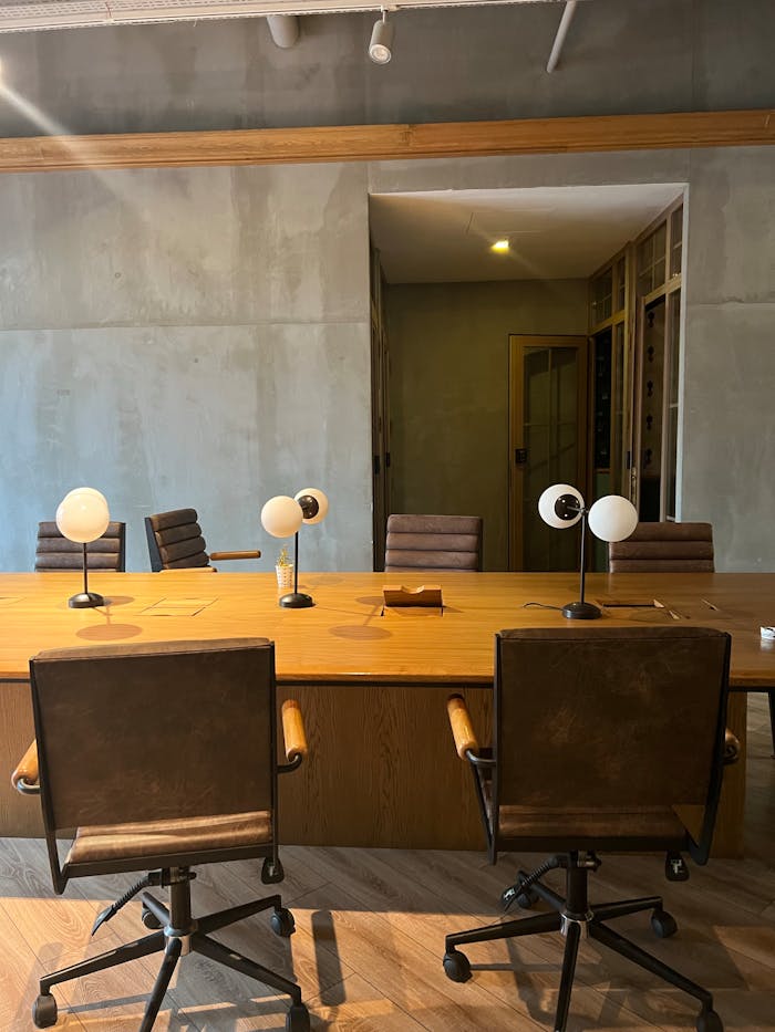 Contemporary office space in İstanbul featuring a wooden table, chairs, and desk lamps against a concrete backdrop.